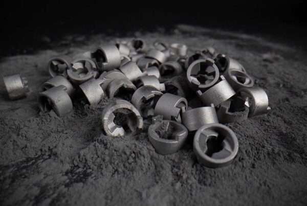 A pile of small metallic parts sits on a surface covered with fine gray dust.