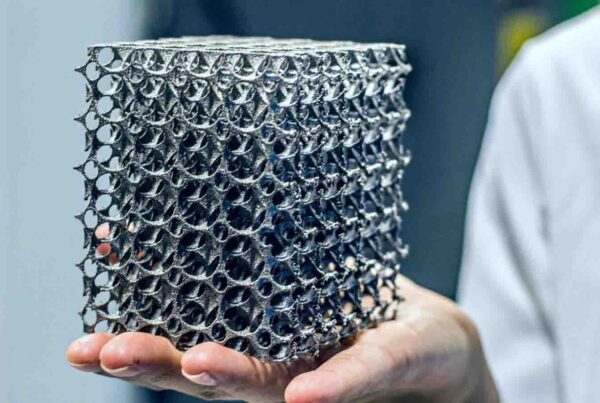 A person in a white lab coat holds a 3D-printed metallic lattice cube with intricate hollow structures, showcasing the tangible results that highlight the pros and cons of 3D metal printing.