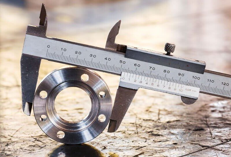 A caliper is measuring the diameter of a metal component with several holes.