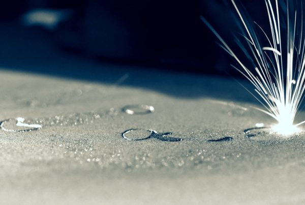 Close-up image of a metal surface with sparks flying from a point of contact where a laser cuts or engraves, highlighted by dramatic lighting.