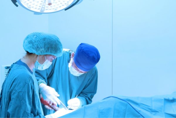 Two surgeons in scrubs and masks perform an operation under bright surgical lights in an operating room.