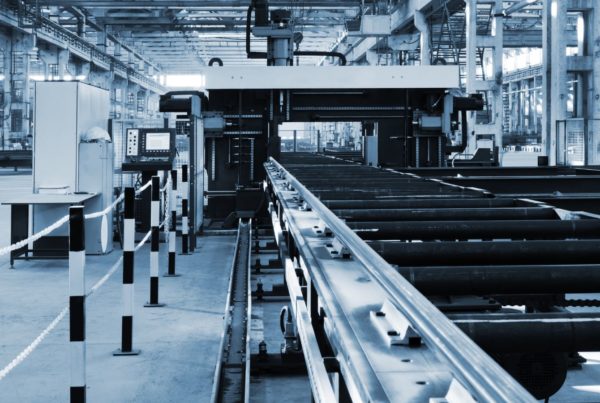 A modern industrial factory with large machinery and conveyor belts handling production of steel pipes, shown in a monochrome blue tone.