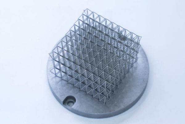 Metal jetting mesh sculpture mounted on a circular base, featuring a complex grid structure, displayed against a plain white background.