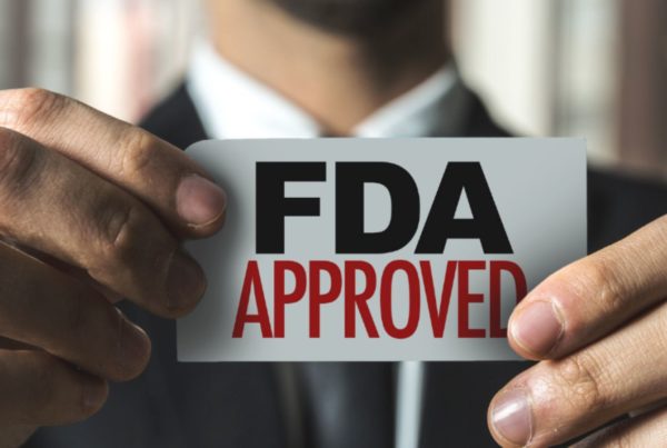 A person in a suit holds up a card with the text "FDA APPROVED" written on it.