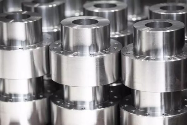 A collection of shiny, cylindrical metal parts with flanges stacked in rows, showcasing precision engineering and manufacturing.