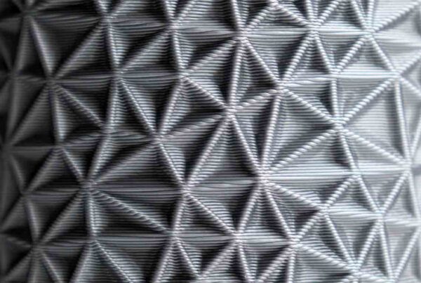 A close-up of a surface with a geometric, triangular pattern, resembling a 3D texture made from interwoven lines. The pattern is repetitive and creates a tactile, structured appearance.