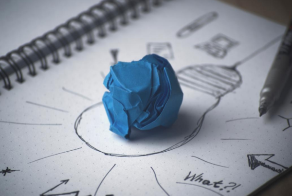 A blue crumpled paper ball on a sketchbook with doodles and a pen nearby, highlighting a creative brainstorming process.