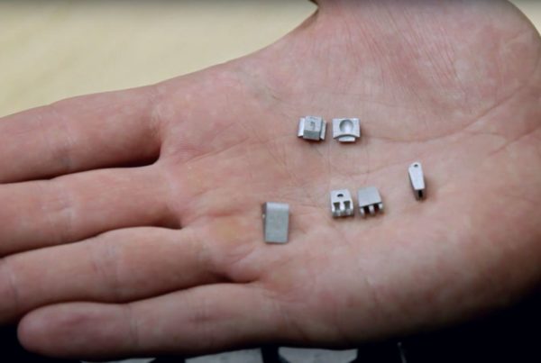 A human hand holding tiny, detailed metal house and car models.