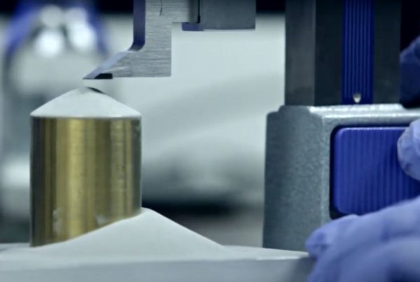 A metal cylinder being tested for pressure resistance in a laboratory setting with a machine applying force from above.