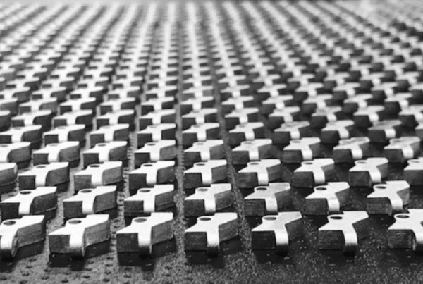 Black and white image of a repetitive pattern of metal crosses arranged in neat rows on a textured surface.