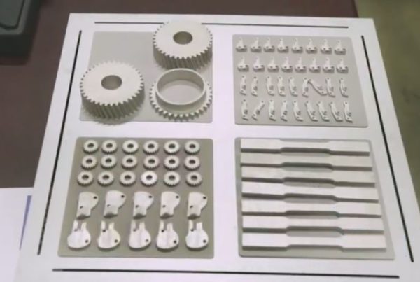 Various 3d-printed mechanical parts displayed on a table, including gears, brackets, and multiple component sets.