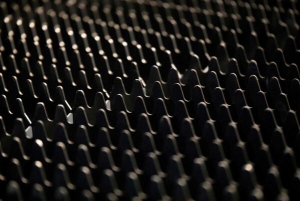 Close-up of a dark textured surface with repetitive, wavy grooves and ridges. The lighting casts subtle shadows, accentuating the undulating pattern.