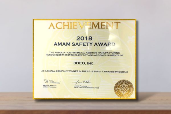 An achievement award certificate for "2018 amam safety award" stands on a wooden surface against a blurred beige background.