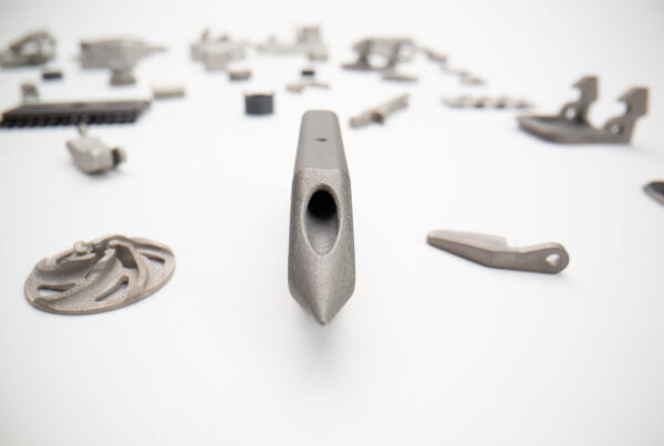 Close-up of a metal object with a hollow center in the foreground, surrounded by various blurred metal components scattered on a white background.