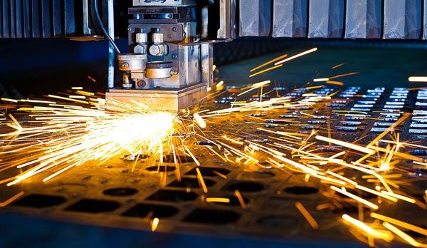 An industrial machine cutting a metal component, emitting bright sparks across a metal grid surface.