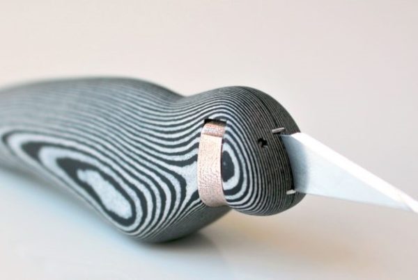 A close-up of a stylized bird sculpture made from layered black and white material using 3D printing, featuring a pointed white beak.