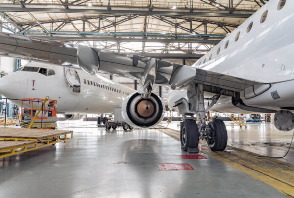 Two white airplanes undergoing maintenance inside a hangar. The view focuses on the landing gear and engines of the aircraft. The area, equipped with scaffolding and various tools, is a hub of aerospace manufacturing precision.