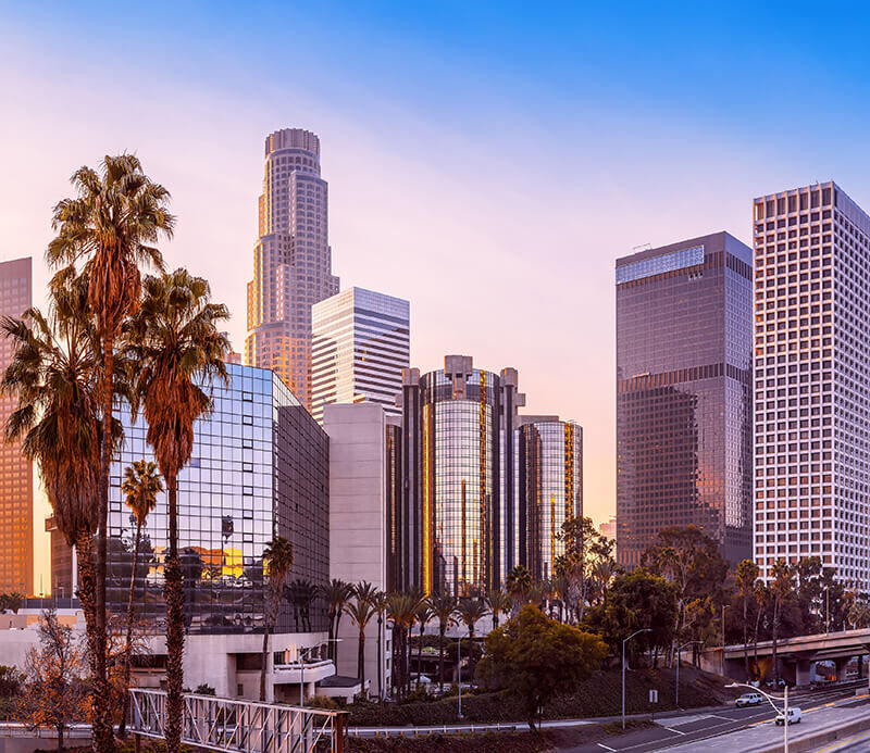 Panoramic view of a cityscape with tall modern buildings, palm trees, and an empty highway in the foreground during a rapid sunset just like what you might see at TCT 2024.