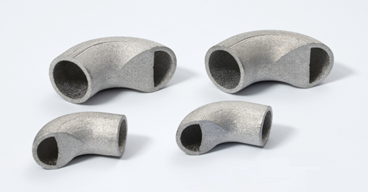 Four metallic elbow pipe fittings of varying sizes are arranged on a white surface, showcasing the precision craftsmanship often seen in aerospace applications.