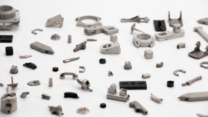 A collection of various small, metal mechanical parts, seemingly ideal for 3D printing, scattered on a white surface.