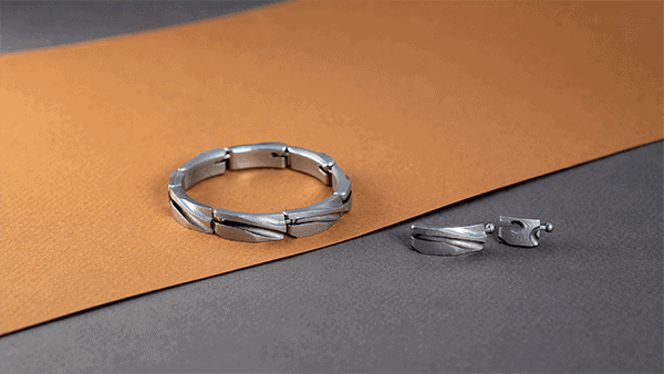 A silver bracelet and matching silver earrings, crafted using 3D printing metal techniques, are placed on a surface with brown and gray backgrounds.