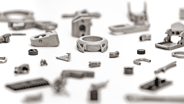 Various small metallic parts, possibly created through 3D printing metal techniques, are scattered against a white background.